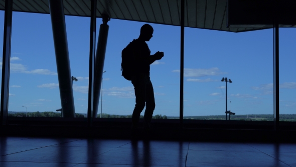 Young Man With a Backpack Standing In An Airport Lounge And Enjoy Your Smartphone.