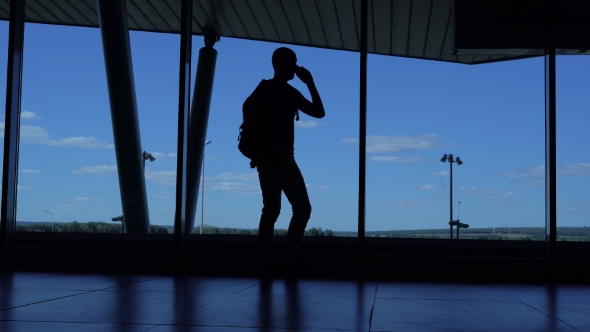 Young Man With a Backpack Standing In An Airport Lounge And Talking On The Phone.