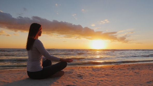 Young Woman With Long Hair Sitting On The Beach At Sunset, Meditating