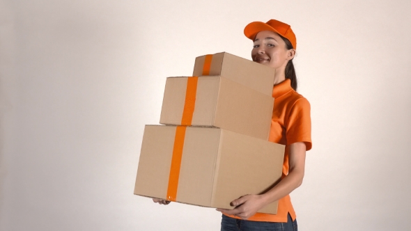 Beautiful Girl In Orange Courier Uniform Delivering a Stack Of Cartons. Light Gray Backround