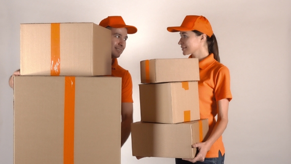 Male And Female Couriers In Orange Uniform Delivering Multiple Cartons. Light Gray Backround