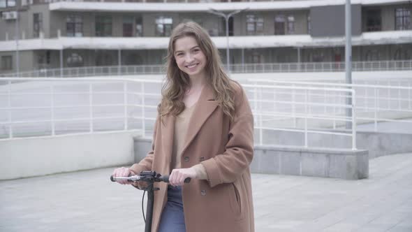 Portrait of Smiling Beautiful Girl Posing with Scooter Outdoors on Cloudy Day. Middle Shot of