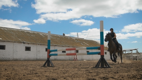 Young Woman Jumps Horse Over An Obstacle During Her Training In An Arena