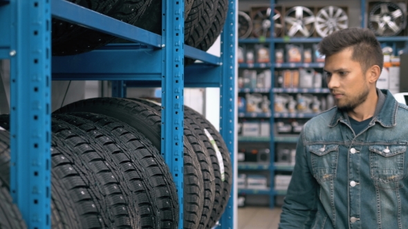 Smiling Man Auto Mechanic Carrying New Tire In Tire Store Choosing For His Car alt