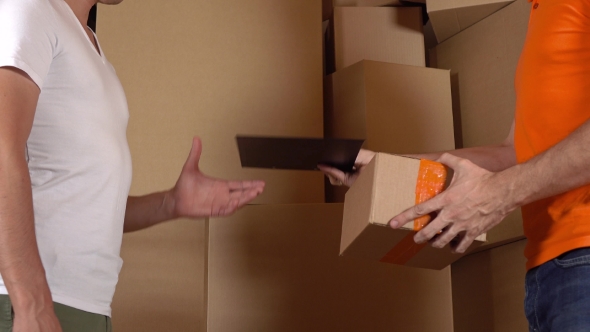 Store Assistant In Orange Uniform Giving a Box To a Customer. Cartons Background,  Studio Shot