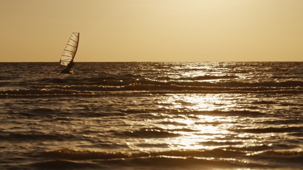 Windsurfer Floats On a Board With a Sail At Sunset