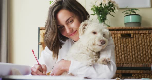Caucasian woman drawing working from home and cuddling her pet dog