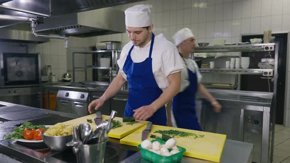 Overworked Caucasian Man in Apron and Cook Hat Rubbing Forehead Looking Away with Colleague Passing