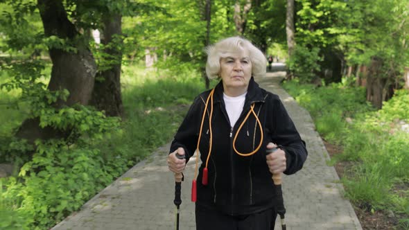 Active Senior Old Woman Training Nordic Walking with Ski Trekking Poles in Park