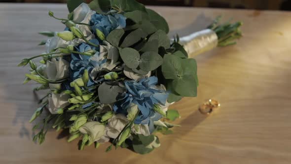 Wedding Rings Lie Near Beautiful Wedding Bouquet on the Wooden Table