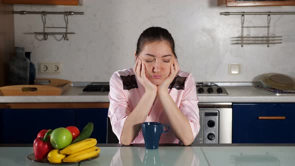 Girl Sits at Table with Cup of Coffee and Falls Asleep