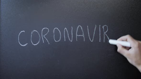 Hand writing word coronavirus on chalkboard. Covid-19. Pandemia.