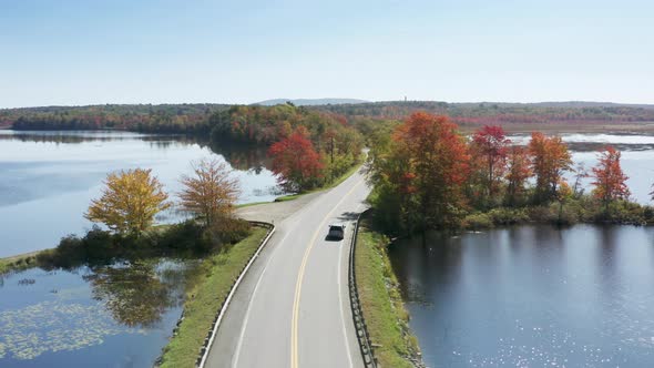 Aerial View Electric Car Driving on Country Road Along Lake Sunny Fall Day