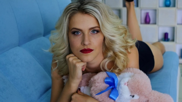 Charming Blonde Lying On The Sofa With a Soft Toy In Her Hands