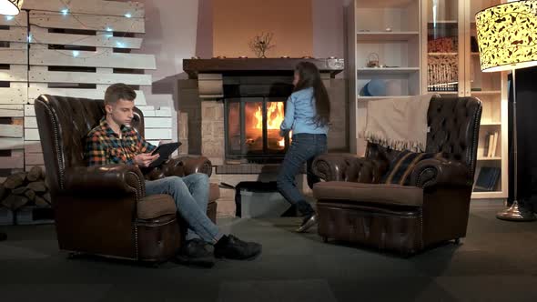 Brother and Younger Sister Spending Free Time Near the Fireplace in Big Cozy Living Room