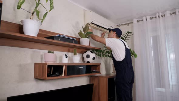 Male Handyman in Overalls Repairs or Cleans the Air Conditioner in the Apartment