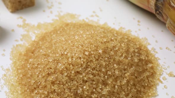  Heap of cane sugar close up and sugar cubes and sugar cane at the background