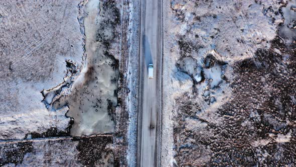 Aerial top down shot of van driving on snowy road in icelandic landscape near Mount Búlandstindur