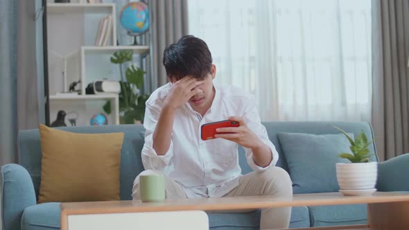 Asian Man Being Upset Losing Game On Smartphone While Sitting On Sofa In The Living Room