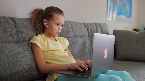Cute Primary School Child Girl Studying with Laptop at Home Sit on Sofa