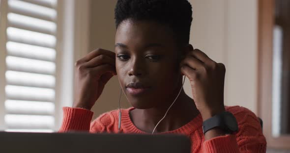 African american woman wearing earphones using laptop while working from home