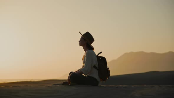 Attractive girl in a hat sitting on the seashore at sunset