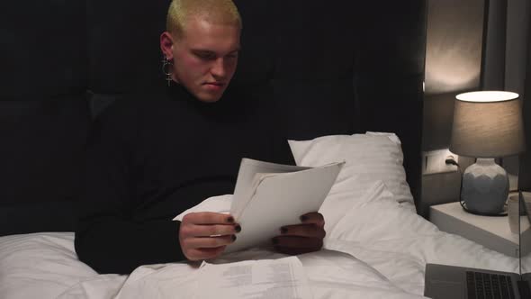 Handsome Homosexual Man Working with Documents on Bed Before Going To Sleep at Home