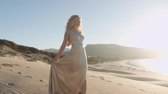 Beautiful Woman In Gold Walking Along Sandy Beach