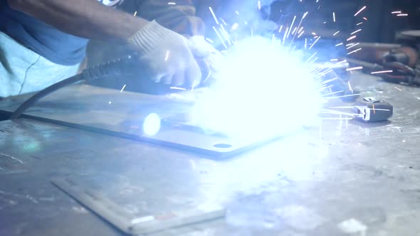 Welder at Work. Worker Welds Metal Parts. Welding Process, Sparks, Flame, Smoke.