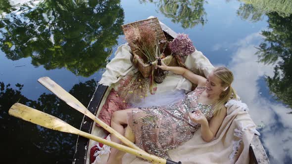 Luxury woman laying in rowboat smiling cheeky at camera and drinking champagne