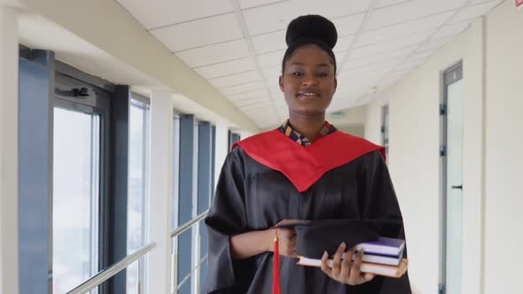 African American Female Graduate in Mantle Stands with a Diploma in Her Hands and Smiles