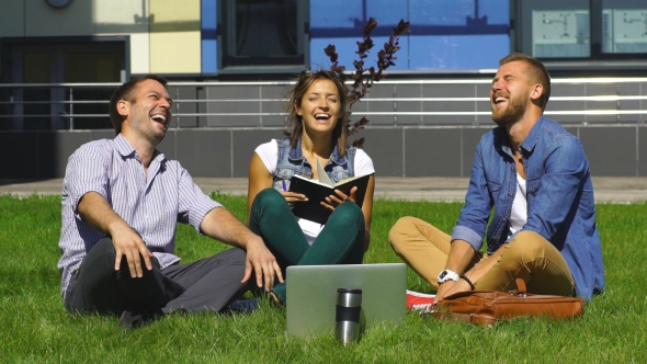 Happy Students Sitting On The Lawn And Laugh