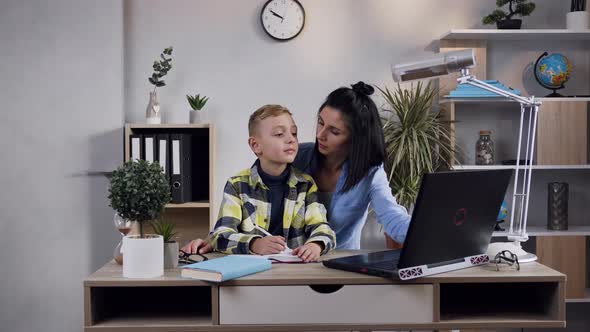 Brunette Woman which Sitting at the Table with Her Teen Son and Working with Computer