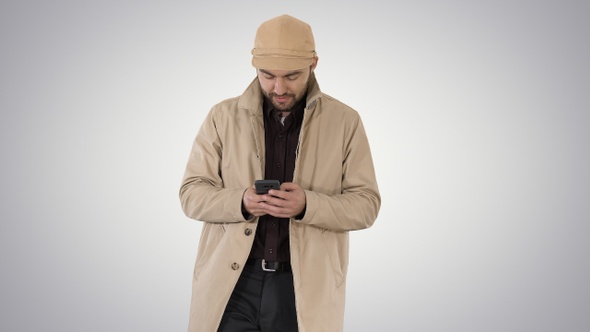 Young handsome man in cloak messaging with phone on gradient