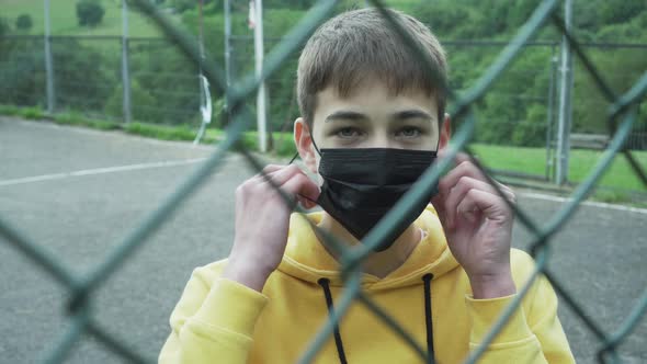 Recovered patient removes a medical mask behind an iron chain-link fence