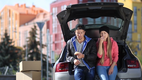 Smiling Couple Sitting In Trunk Of Modern Car alt