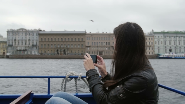 Girl Sitting In a River Bus On The Go Taking Photos Of Architecture On a River Quay. A Seagull Is