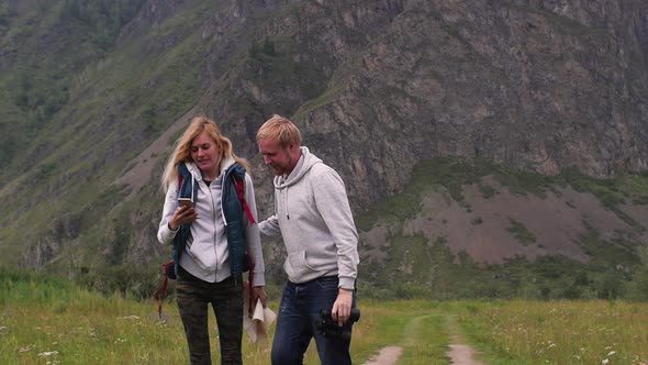 Young Couple with the Phone on a Background of Mountains. Mobile Communication in the Mountains