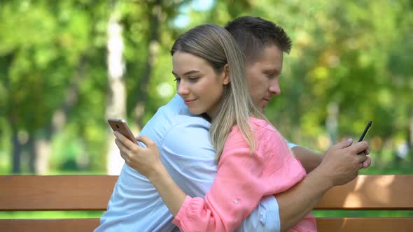 Young Couple Hugging at Park, Chatting on Smartphones, Lack of Communication