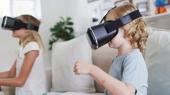 Caucasian brother and sister gesturing while using vr headset sitting on the couch at home