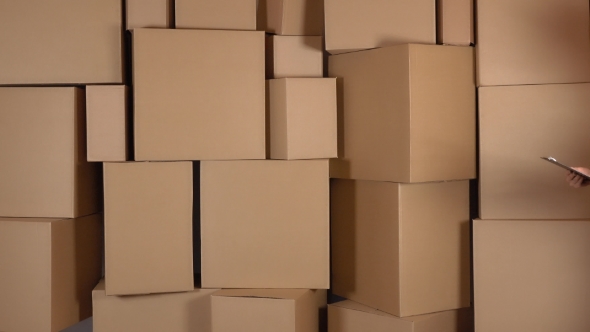 Beautiful Female Warehouse Worker In Orange Uniform Walking Against Brown Cardboard Boxes Backround