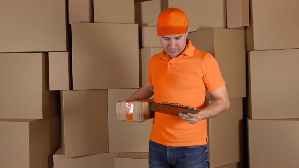 Man In Orange Uniform Delivering Heavily Damaged Parcel To Customer. Brown Cartons Background