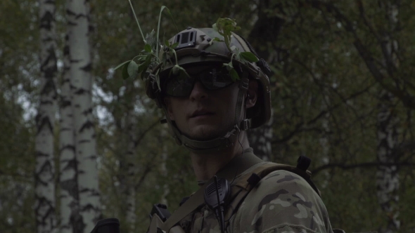A Soldier In a Helmet And Glasses Stands On a Forest Background