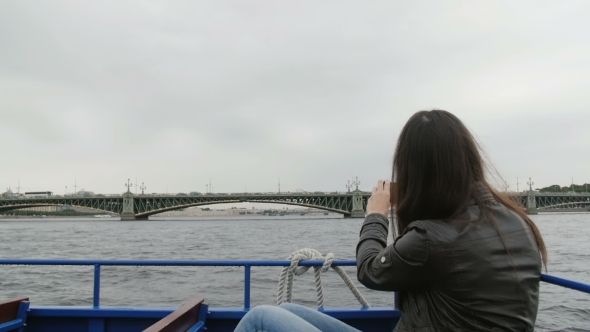 Young Brunette Woman Sightseeing In a River Bus. Taking Photos On a Smartphone Of a Bridge 