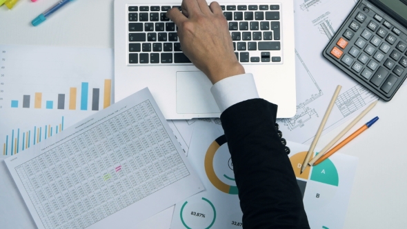 Businessman Working At Office Desk On His Laptop And Financial Reports