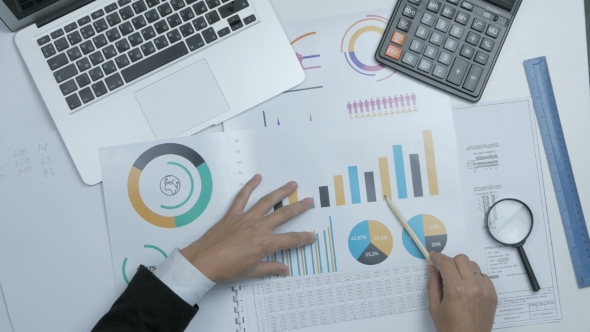 Businessman Working at Office Desk on His Laptop and Financial Reports