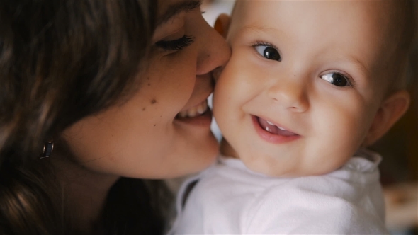 Young Happy Mother Holding Her Newborn Child And Kissing. Family At Home. Beautiful Smiling