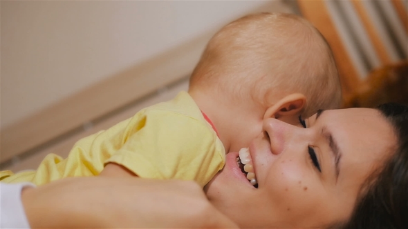 Young Happy Mother Holding Her Newborn Child And Throws Up. Family At Home. Beautiful Smiling Mom