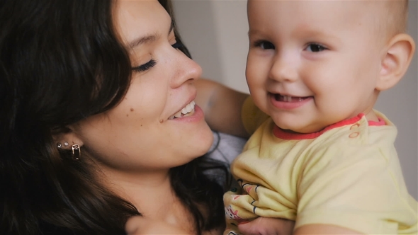 Young Happy Mother Holding Her Newborn Child. Family At Home. Beautiful Smiling Mom And Happy Baby alt