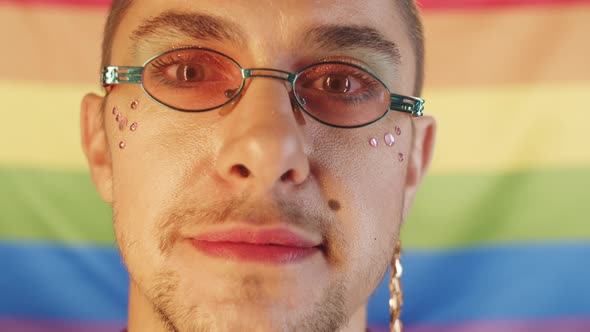 Happy Gay Man with Makeup Smiling at Camera against Rainbow Flag